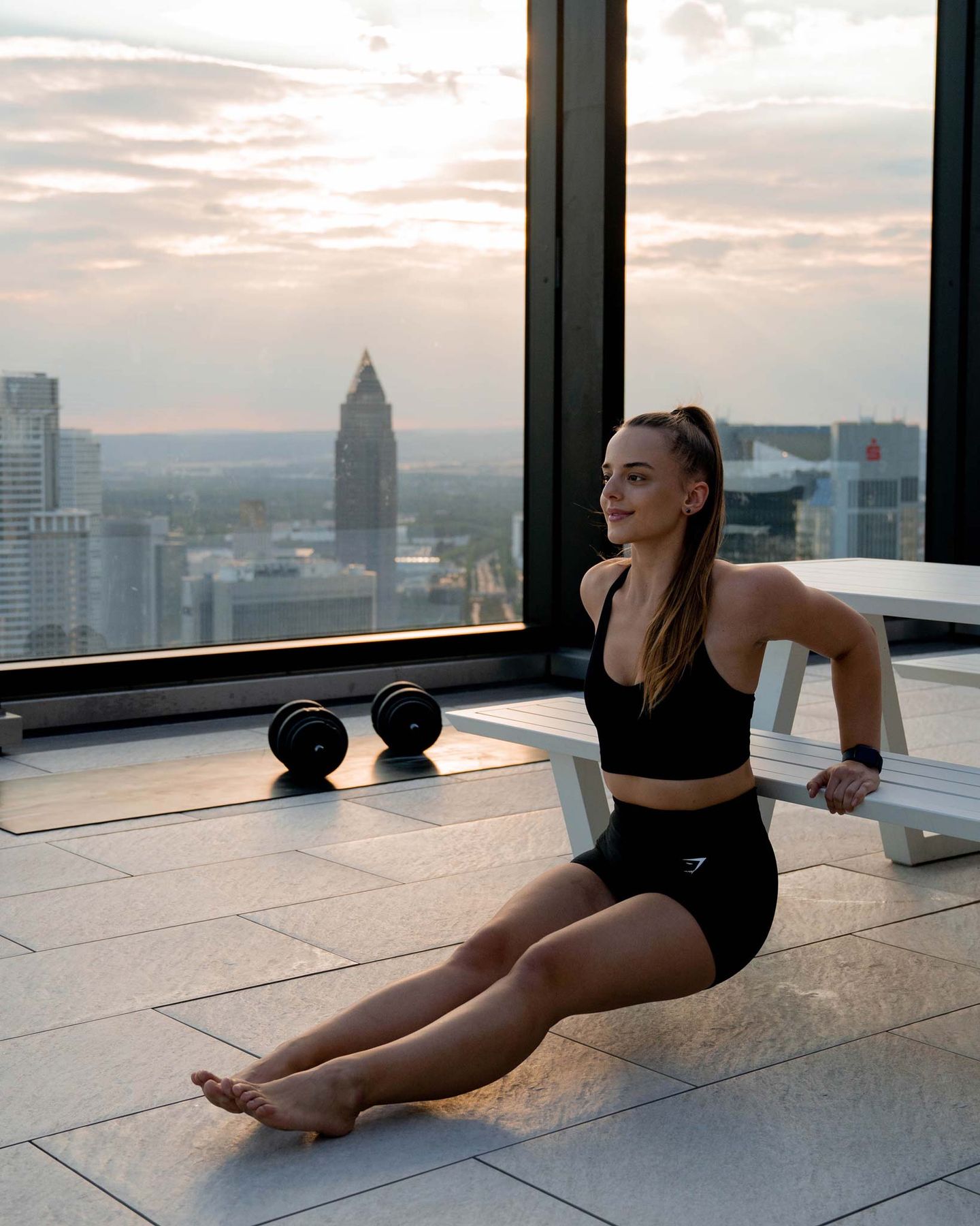 Lili Nowicki sitzt in Sportkleidung vor einer Fensterfront mit Blick über die Frankfurter Skyline